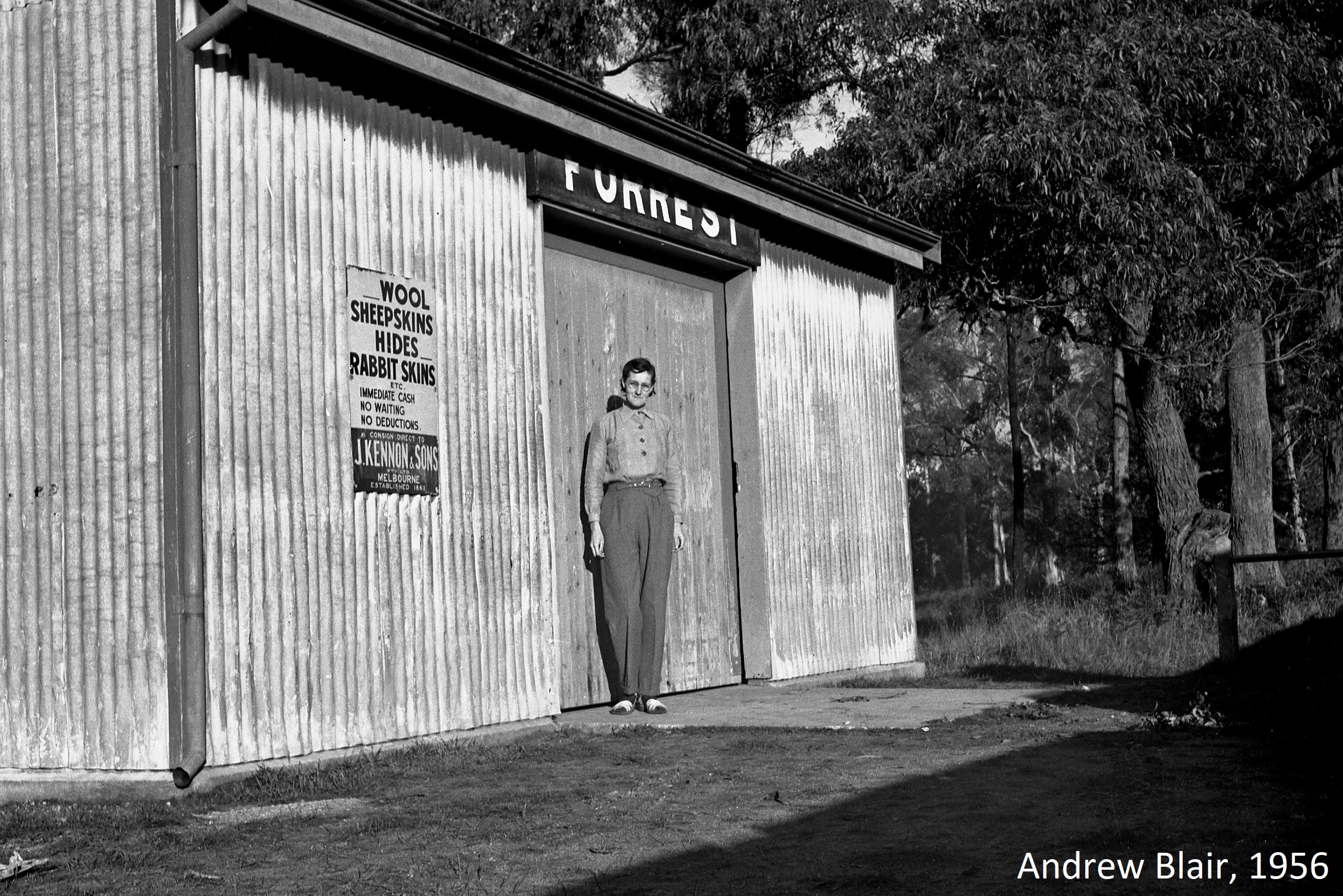 Woman wearing trousers and long sleeved blouse standing in front of goods shed on Forrest Railway platform.