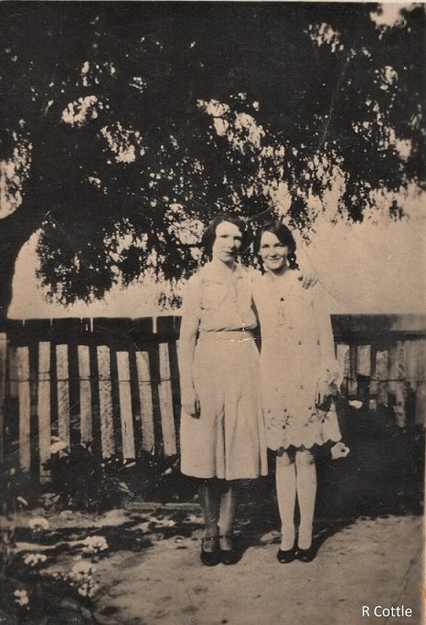 Woman and her daughter standing in front of fence and under tree. 